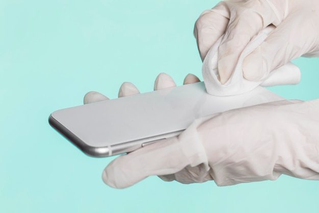 Foto gratuita manos con guantes quirúrgicos desinfectando smartphone