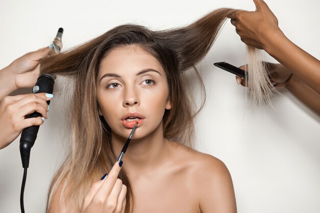 Manos haciendo maquillaje y peinado de joven bella mujer