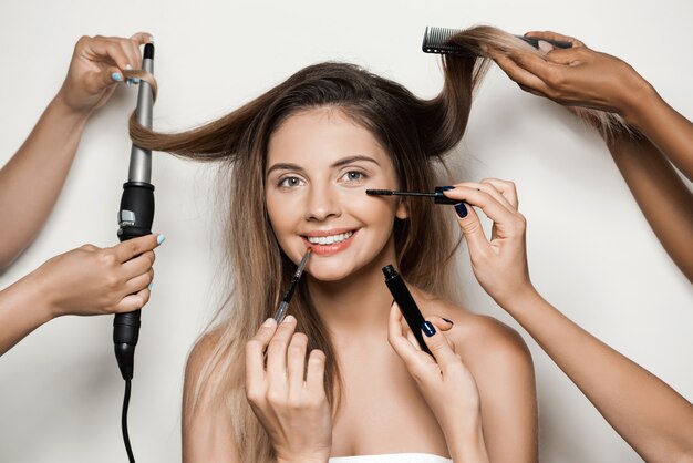 Manos haciendo maquillaje y peinado de joven bella mujer