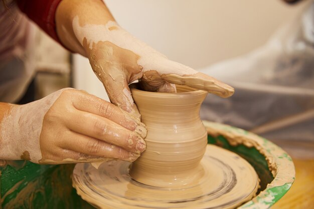 Las manos del hombre están moldeando un jarrón en un lugar de trabajo de cerámica