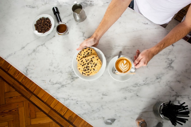 Manos de hombre con galletas y un capuchino en el mostrador