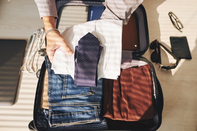 Manos de hombre irreconocible empacando maleta para viajar