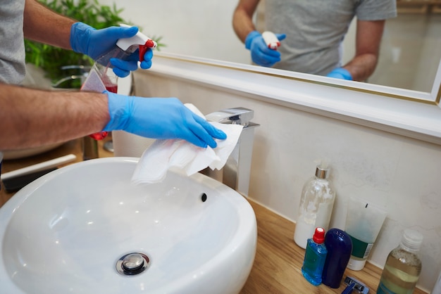 Manos del hombre limpiando el fregadero en el baño.