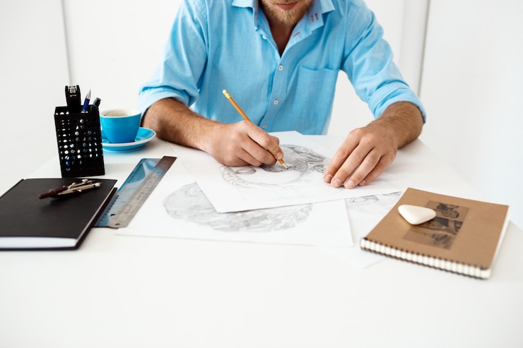 Foto gratuito manos del hombre de negocios joven que se sienta en la tabla con el retrato del dibujo de lápiz. interior de oficina moderno blanco.
