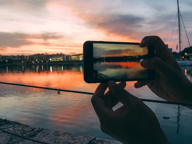 Manos de hombre tomando una foto con teléfono móvil de una puesta de sol