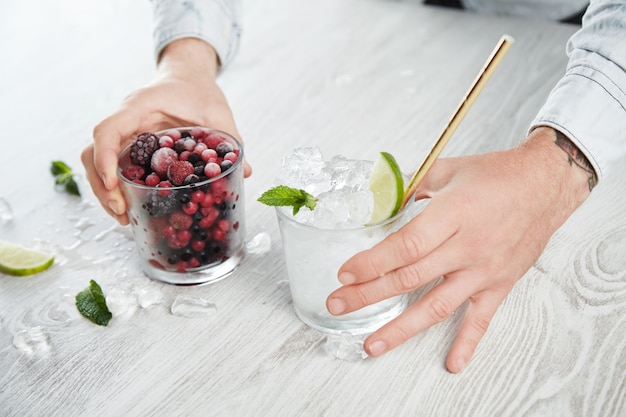 Las manos del hombre de vista cercana lateral sostienen vasos con bayas congeladas y cubitos de hielo con cal