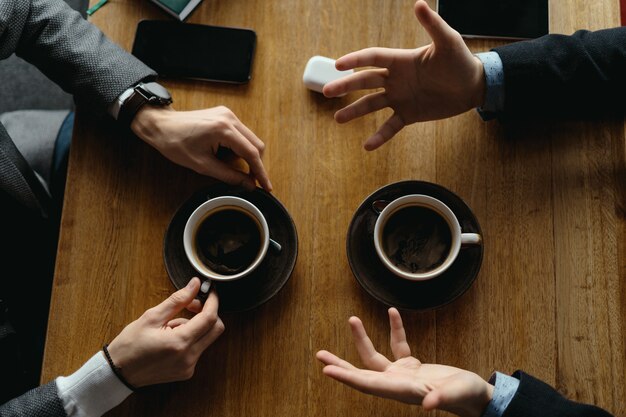 Manos de hombres gesticulando mientras sostienen tazas de café