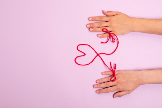 Manos humanas conectadas con hilo rojo en forma de corazón