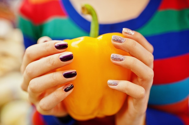 Manos con manicura de ropa de niña en suéter de color perforando pimiento rojo