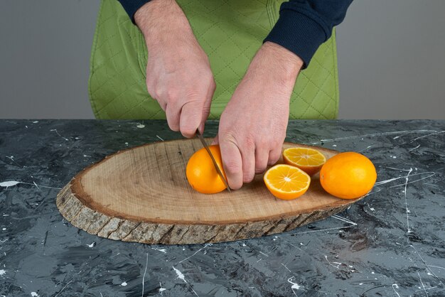 Manos masculinas cortando jugosa mandarina en mesa de mármol.