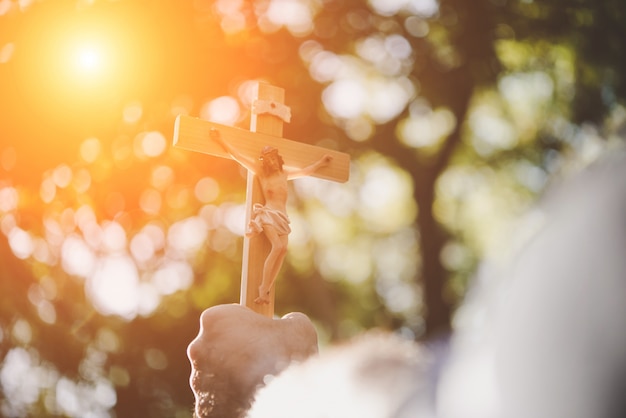 Las manos masculinas que sostienen la cruz de madera de Jesús en el cielo con el fondo de la naturaleza.