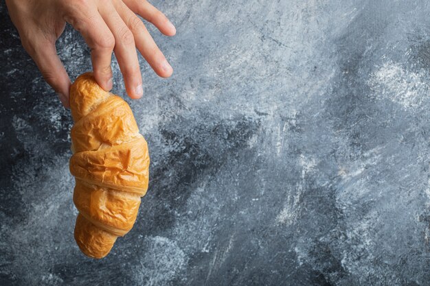 Manos masculinas sosteniendo croissant fresco sobre fondo de mármol