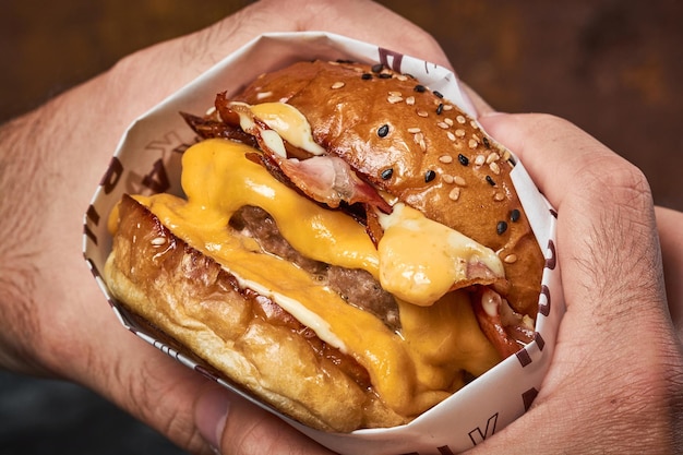 Manos masculinas sosteniendo una deliciosa hamburguesa doble con queso