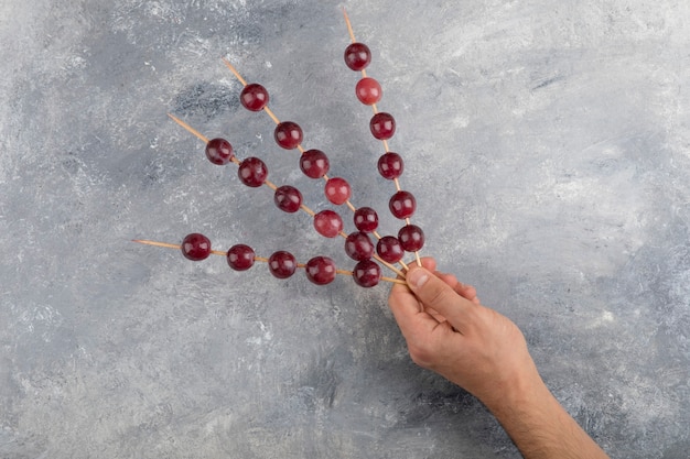 Manos masculinas sosteniendo palos de uvas rojas sobre fondo de mármol.