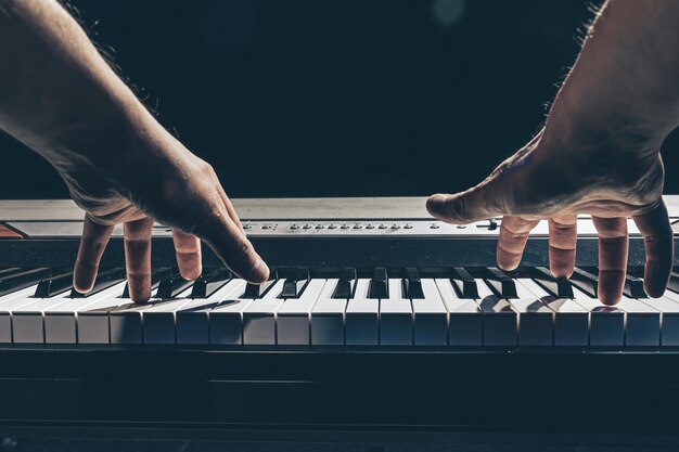 Manos masculinas tocan las teclas del piano en la oscuridad