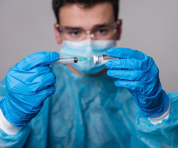 Manos del médico insertando la jeringa en el vial de la vacuna Covid-19