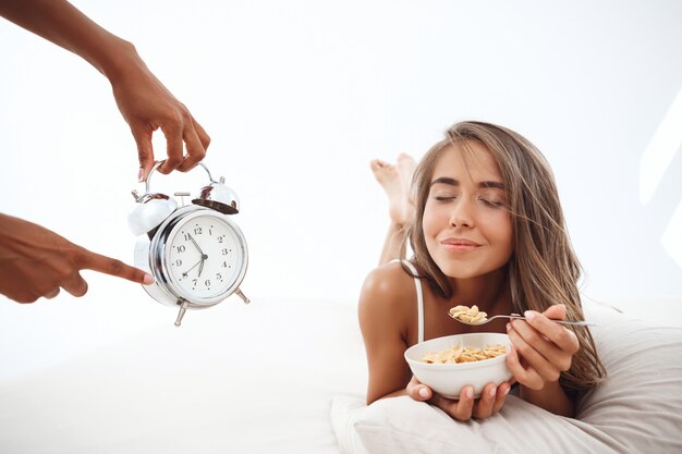 Manos mostrando la hora en el despertador a hermosa mujer acostada en la cama