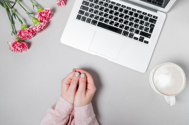 Manos de mujer con café y claveles de flores portátiles sobre fondo blanco Fondo de espacio de trabajo de primavera Vista superior