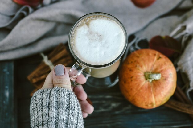 Manos de mujer con café con leche picante de calabaza en una tabla de madera con un suéter