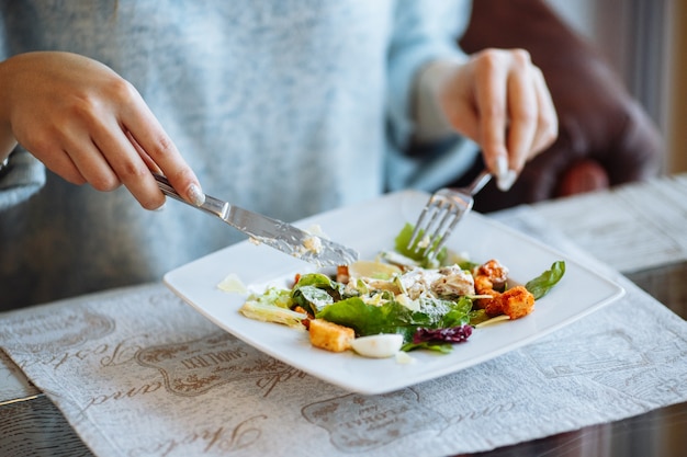 Manos de mujer con ensalada César en la mesa en el restaurante