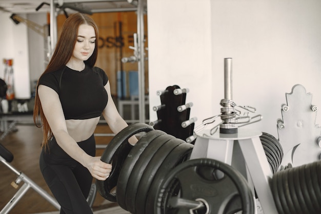 Manos de mujer fuerte sosteniendo el disco de la barra y poniéndolo en los discos de hierro en el gimnasio. La mujer joven muscular sostiene el disco de hierro de la barra.