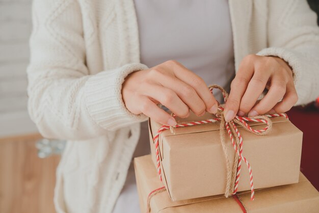 Manos de mujer irreconocible atando regalos de Navidad con hilo decorativo