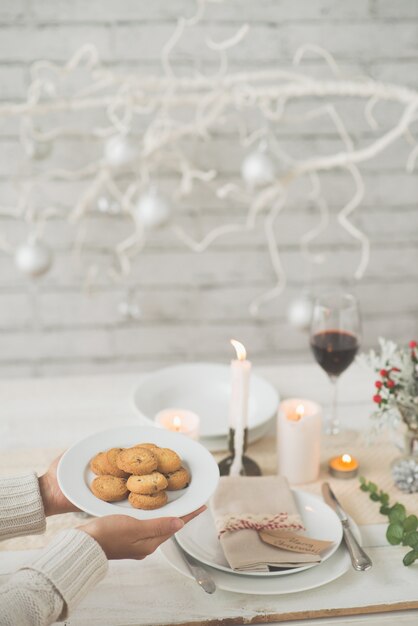 Manos de mujer irreconocible llevando plato de galletas a la mesa de Navidad