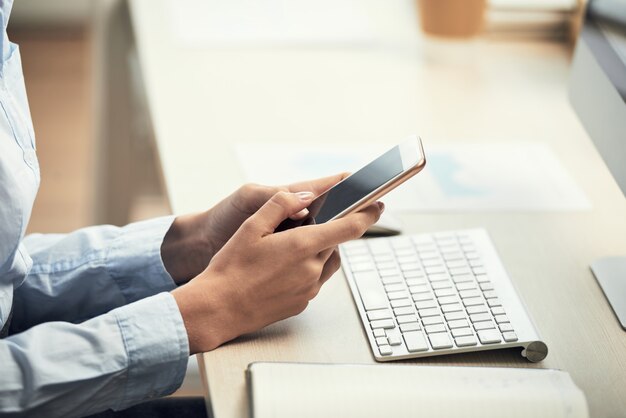 Manos de mujer irreconocible con smartphone en el escritorio en la oficina