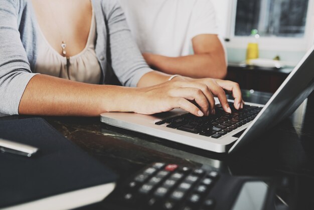 Manos de mujer irreconocible trabajando en la computadora portátil en casa y hombre sentado a continuación