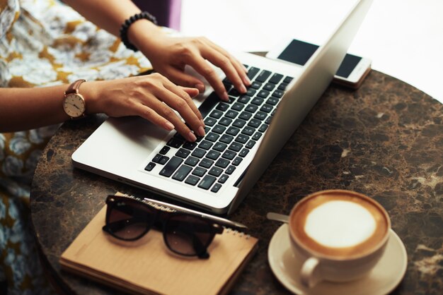 Manos de mujer joven irreconocible usando laptop en café