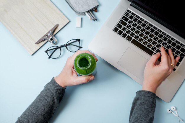 Manos de mujer con Laptop y batidos verdes con manzana en la mesa azul Vista superior plana