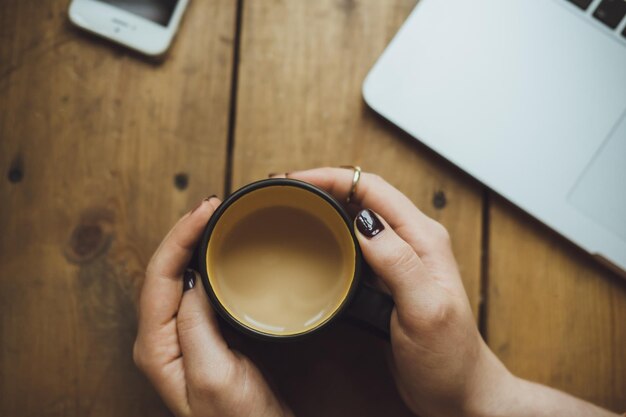 Manos de mujer con laptop y café en la vista superior de la mesa