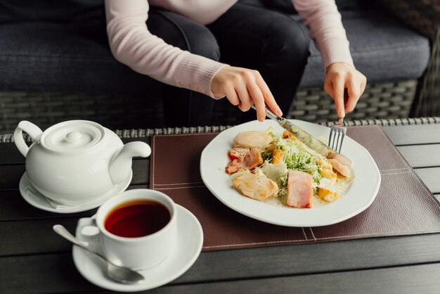 Manos de mujer listas para comer ensalada César y beber té en el restaurante