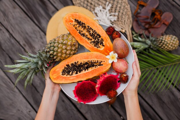 Manos de mujer con plato grande de frutas exóticas frescas.