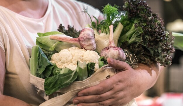 Manos de mujer sosteniendo brócoli orgánico maduro fresco, ensalada con verduras y verduras en una bolsa de algodón en el mercado de agricultores de fin de semana