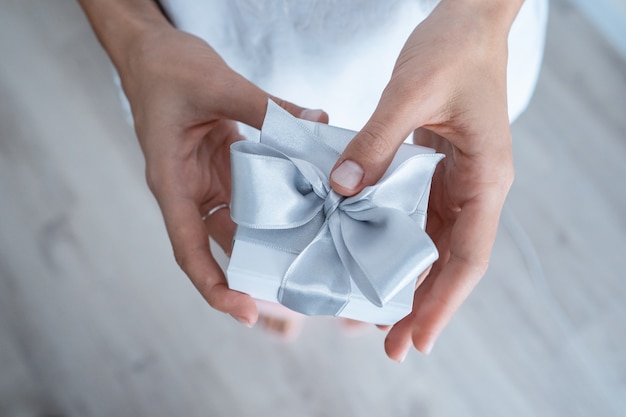 Manos de mujer sosteniendo caja de regalo con lazo blanco, primer plano