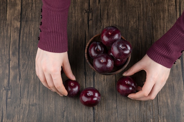 Manos de mujer sosteniendo un cuenco de madera con ciruelas moradas saludables.