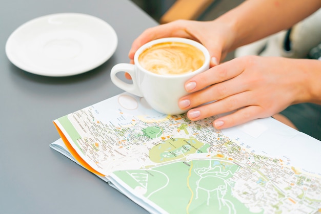 Las manos de la mujer sostienen la taza de café sobre el mapa en la tabla. Chica viaja a las Islas Canarias y busca un nuevo lugar para visitar. Día soleado en un café de la calle.