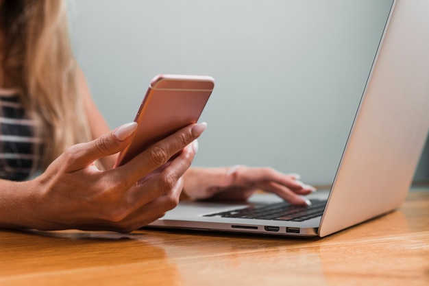 Manos de mujer con teléfono y computadora portátil