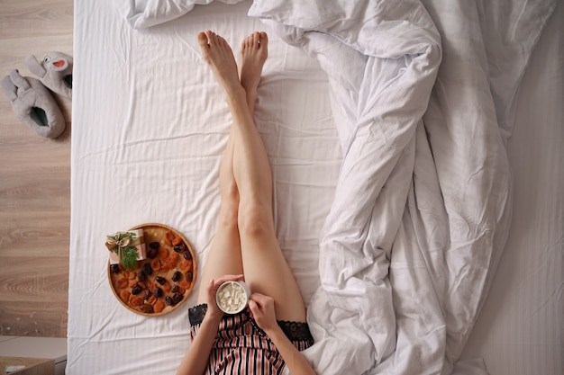 Las manos de las mujeres sostienen café con malvaviscos en sábanas blancas con luces. Sorpresa de la mañana