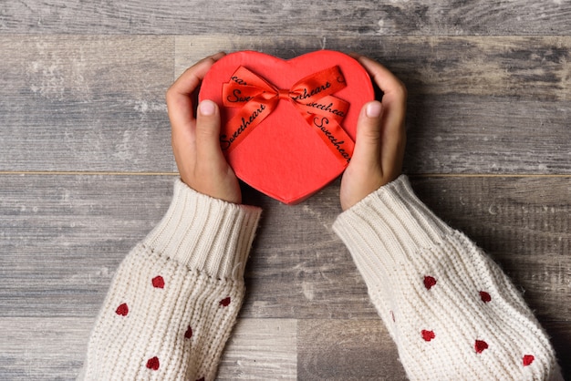 Manos de niña pequeña sujetando una caja de regalo con forma de corazón