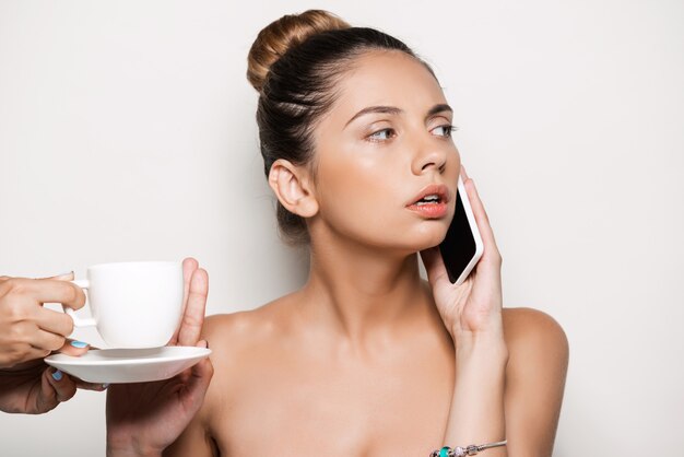Manos ofreciendo una taza de café a una mujer hablando por teléfono