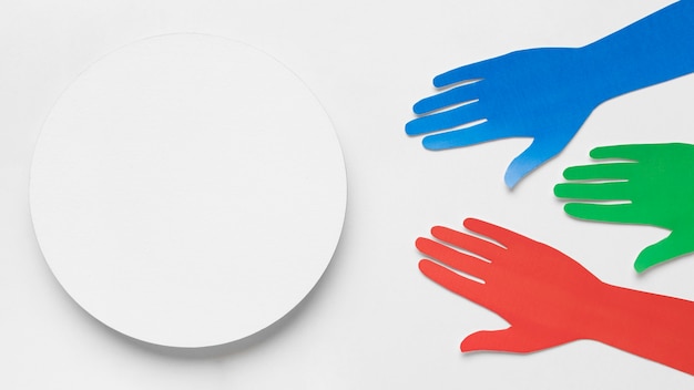 Manos de papel de diferentes colores junto a un círculo blanco