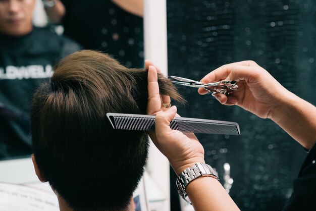 Manos de peluquero irreconocible cortando el cabello del cliente masculino en el salón