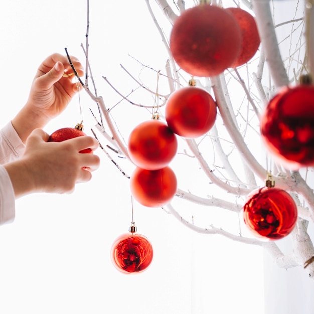 Manos poniendo bolas de navidad en árbol