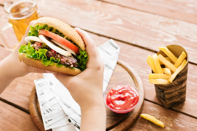 Manos de primer plano de alto ángulo sosteniendo hamburguesa con hamburguesa con papas fritas