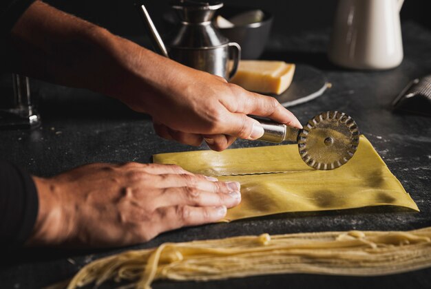 Manos de primer plano con cortador de pizza y utensilios