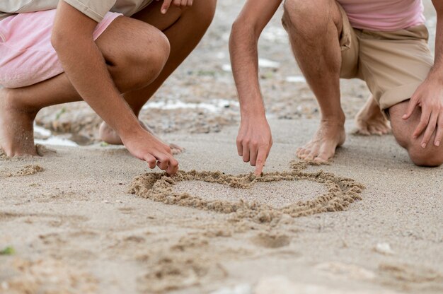 Manos de primer plano dibujo corazón sobre arena.