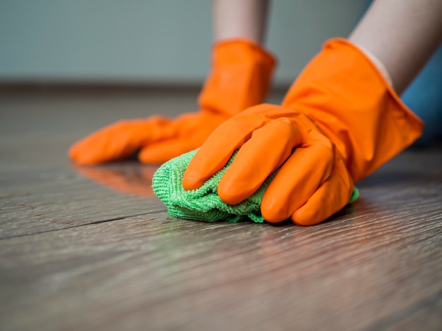 Manos de primer plano con guantes de goma limpiando el piso