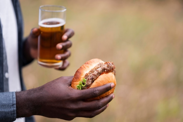 Manos de primer plano sosteniendo cerveza y hamburguesa